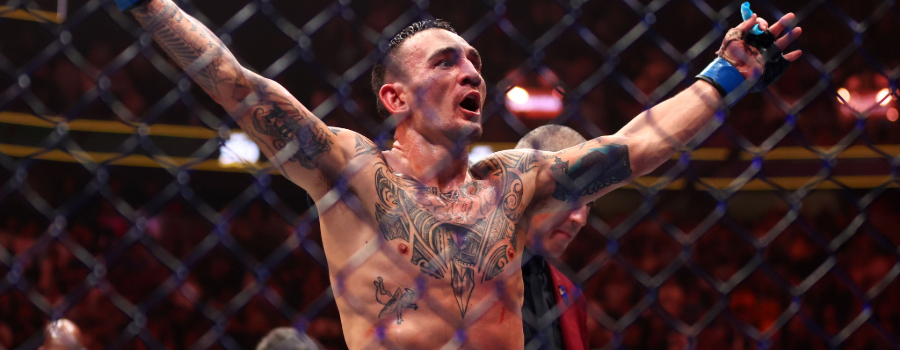 Max Holloway celebrating victory in the UFC octagon, arms raised, showing tattoos and wearing MMA gloves, with the cage and crowd in the background.